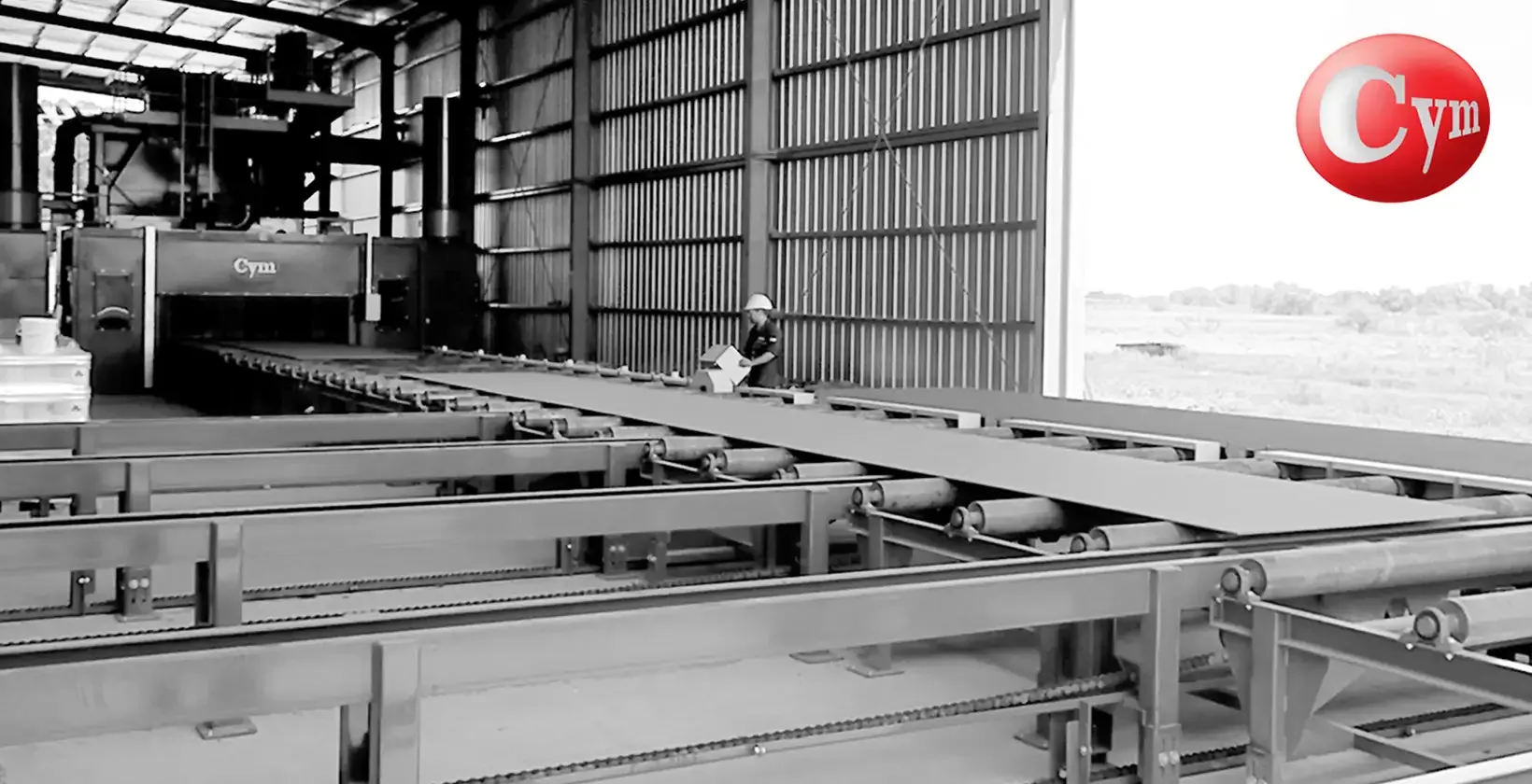 CYM CH 2.5H plate blaster exit transfer – transverse roller table with blasted plates, CYM machine background, operator supervising · Astillero Paraná Sur, Argentina