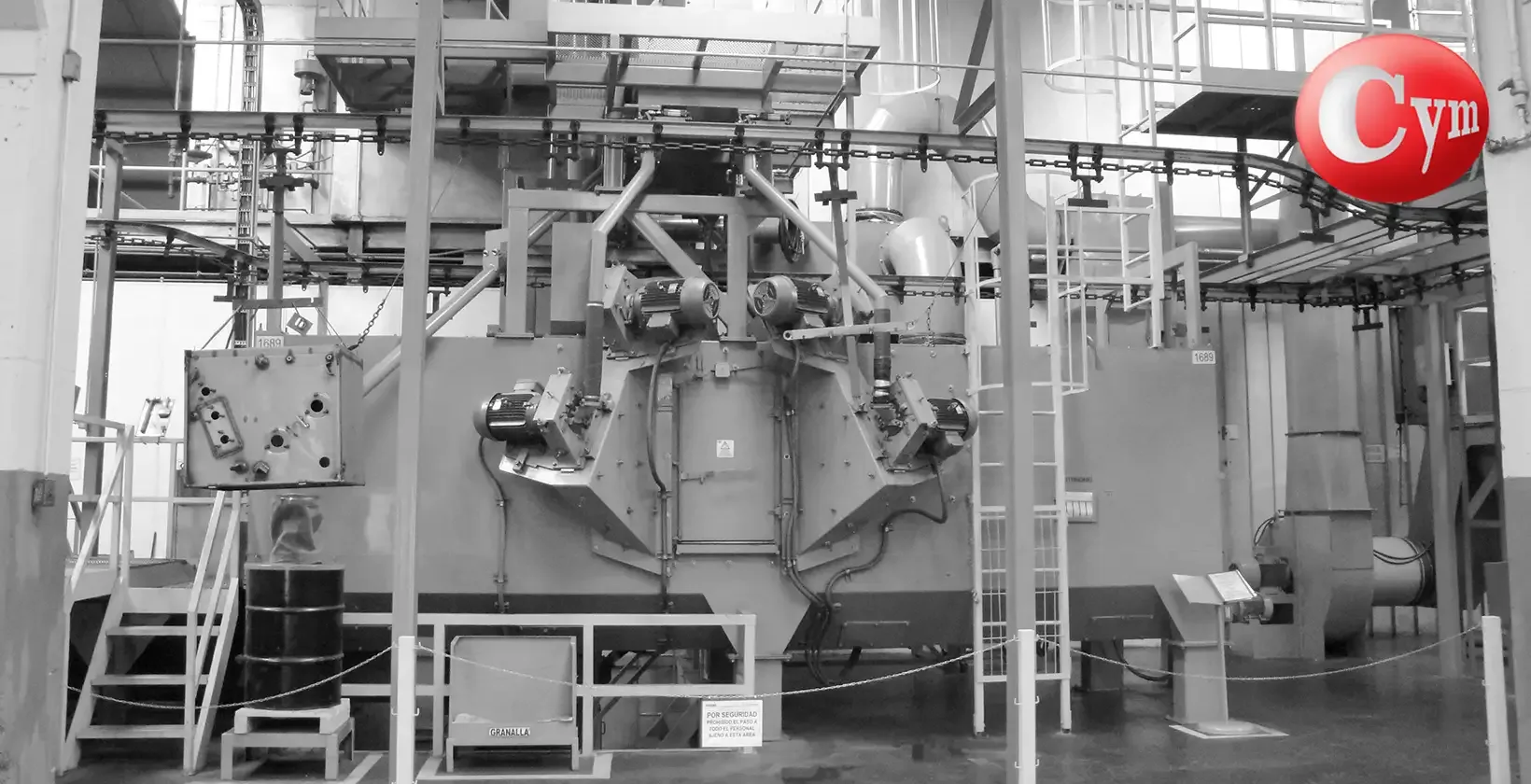 Interior de cabina granalladora CYM EST 15x15 – transformador eléctrico suspendido en cadena aérea durante proceso de granallado
