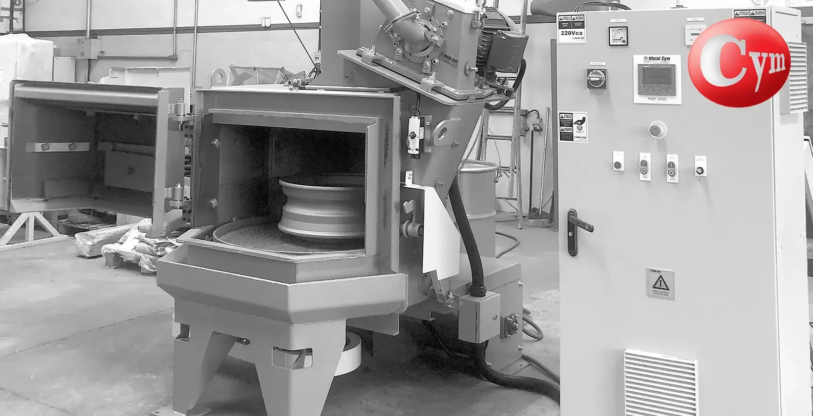 CYM rotary table blast machine — aluminum wheel on table — hinged door open — CYM Materiales control panel — Argentina